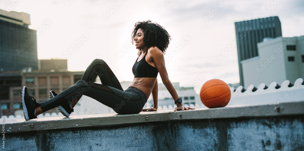 Wall mural Female athlete relaxing on the rooftop fence