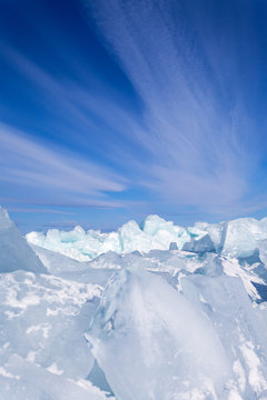 Blue ice blocks and hummocks under a blue sky with stratus clouds. Natural winter ice cold background. Lake Baikal in February