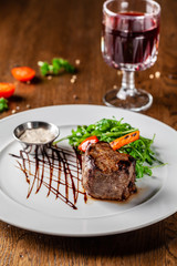 Georgian cuisine. Juicy beef steak, veal steak on a white plate with roasted rocket, grilled vegetables and sauce. On the table is a glass of red pomegranate wine. Serving dishes in the restaurant
