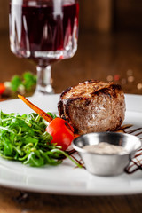 Georgian cuisine. Juicy beef steak, veal steak on a white plate with roasted rocket, grilled vegetables and sauce. On the table is a glass of red pomegranate wine. Serving dishes in the restaurant