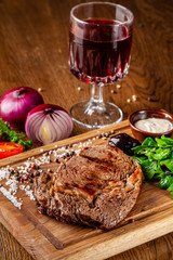 Italian cuisine. Juicy beef meat, veal steak on a wooden board with spinach, prunes and French mustard sauce. On the table is a glass of red pomegranate wine. Serving dishes in the restaurant