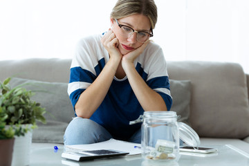 Worried young woman looking her savings while sitting on sofa at home.