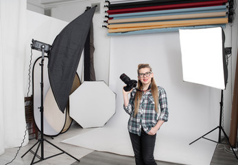 Happy girl professional photographer in photo studio with digital SLR camera in hands