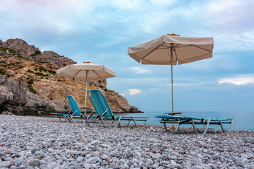 Sunbeds and umbrellas on Traganou beach at sunset, Rhodes island, Greece