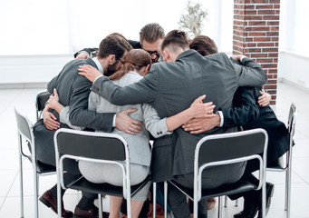 business team sits in a circle and hugs each other