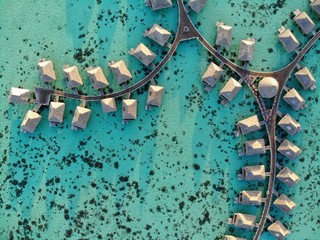 Aerial view of overwater bungalows with thatched roofs in the Moorea lagoon in French Polynesia - obrazy, fototapety, plakaty