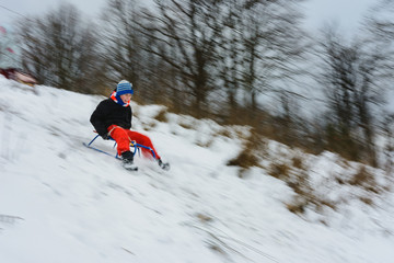 Fototapeta na wymiar the boy descends from the hills in the sled, the movement is blurred