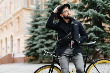 Portrait of urban hipster man in glasses and hat posing with bicycle on the street