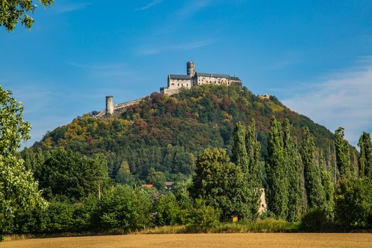 Landscape with green hill in distance and famous medieval castle Bezdez from 13th century standing on top of it, Czech republic, Europe, sunny day, blue sky, brown field in foreground