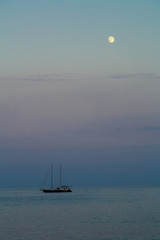 A small yacht with a sail in the sea at dusk in the evening.