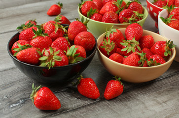 Bowls with strawberries on gray wooden desk.