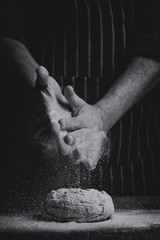 Flour is sprinkled over a ball of dough on a wooden board by hand in artistic conversion