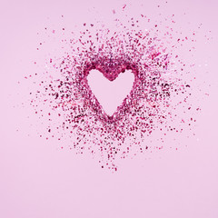 Glitter heart dissolving into pieces on pink background.  Valentines day, broken heart and love emergence concept
