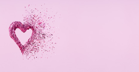 Glitter heart dissolving into pieces on pink background.  Valentines day, broken heart and love...