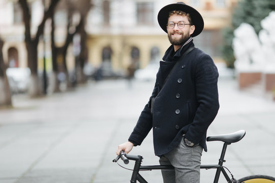 Confident and stylish. Full length of confident young bearded man adjusting eyewear while sitting on his bicycle outdoors - Powered by Adobe