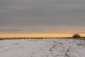 Sunset in cold winter day at the snowy seashore and rocky mole.