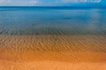 The blue sky is reflected in the clear water of the ocean. Blue water and yellow sand of Koh Samui beach.