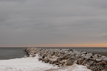 Sunset in cold winter day at the snowy seashore and rocky mole.