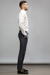 An elegant man in casual business clothes is standing tall with his hands in his pockets on a gray...