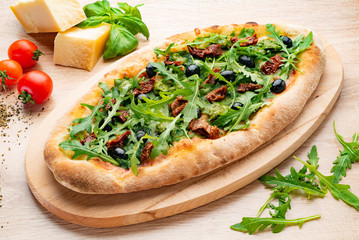 pizza with dried tomatoes and arugula on the wooden board