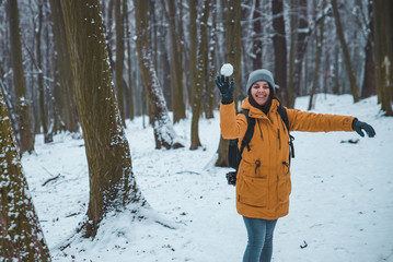 Fototapeta na wymiar smiling young woman throwing snowball in forest