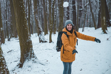 Fototapeta na wymiar smiling young woman throwing snowball in forest
