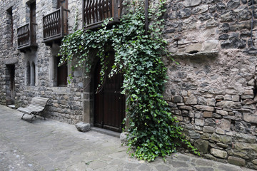 Fototapeta na wymiar A wooden door with green ivy on a stone made house with some wooden balconies in the rural Pyrenees mountains town of Hecho, in Aragon, Spain