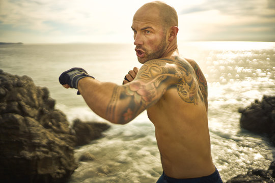 Male athlete with tattoo boxing near ocean