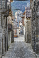 A rural street of a Pyrenees mountain hamlet with stone houses with wooden balconies and dark roofs during winter in Ansó, Aragon region, Spain