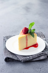 A piece of Japanese cotton cheesecake with mint and strawberry on a white plate. No crust cheesecake. Grey stone or concrete background. Selective focus, copy space. 