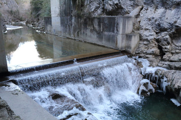 A small waterfall over concrete in the Veral river with grey rock and cold ice stalactites in the Foz de Binies zone, during winter, in Aragon, Spain