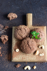 Chocolate cookies for breakfast with mint and  cashew nuts on wooden cutting board. Dark old concrete background. Copy space.
