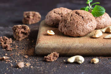 Chocolate cookies for breakfast with mint and  cashew nuts on wooden cutting board. Dark old concrete background. Copy space.