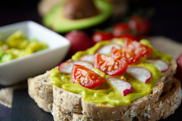 Close-up of toast with avocado, tomato and radish and the ingredients