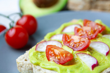 Close-up of toast with avocado, tomato and radish on a plate and the ingredients