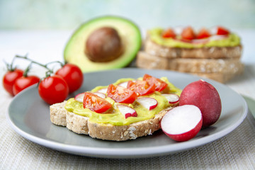 Frontal view of toast with avocado, tomato and radish and the ingredients on a plate