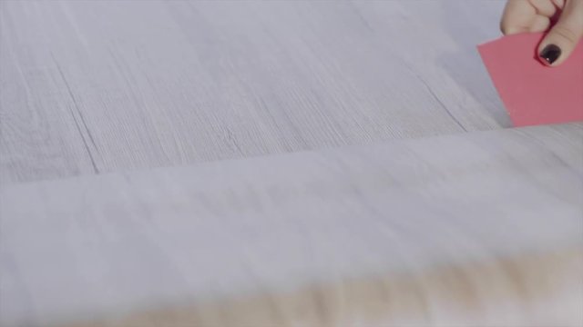 female hand sticking self-adhesive wood film with a scraper