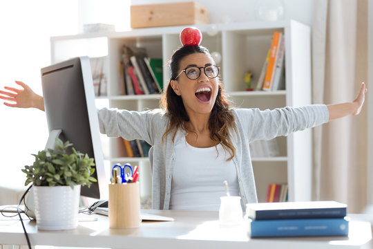 Happy young business woman having fun and holding red apple over her head in the office.