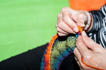 Hand of old woman holding knitting needles and multi colored wool for woolwork of warm sweater for cold winter days close up selective focus 