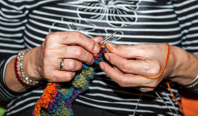 Hand of old woman holding knitting needles and multi colored wool for woolwork of warm sweater for...