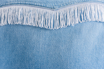Closeup blue jeans texture with white fringe decoration and copy space. Stylish modern clothing.