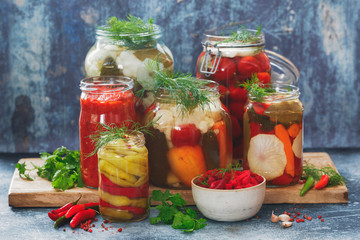 Colorful preserved and marinated seasonal vegetables with herbs on rustic wooden kitchen table