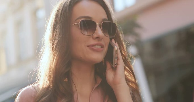 Close up of the pretty young brunette woman in sunglasses talking on the mobile phone and laughing. Outdoor on the sunny day.