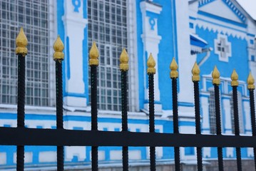 black sharp iron bars of the fence against a blue white wall with windows