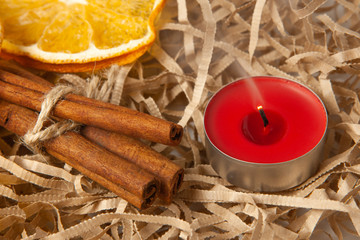 Orange slice and fragrant cinnamon sticks with a red extinguished candle, close-up