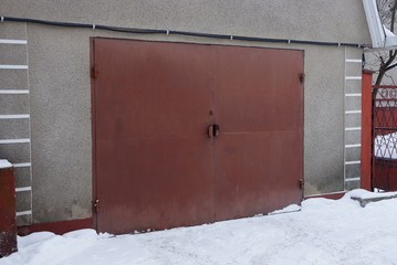 one brown iron gate on the wall of an old garage outside in white snow