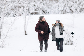 Fototapeta na wymiar Young couple running on a snowy winter field near pine