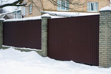 part of a private brown iron fence and a closed gate in white snow outside