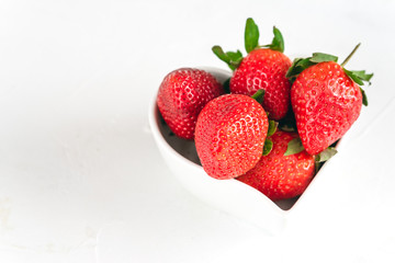 Fresh strawberries in a heart shaped bowl isolated on white background.