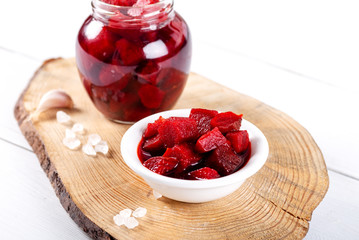 Pickled red betroot in bowl and jar on wooden background.
